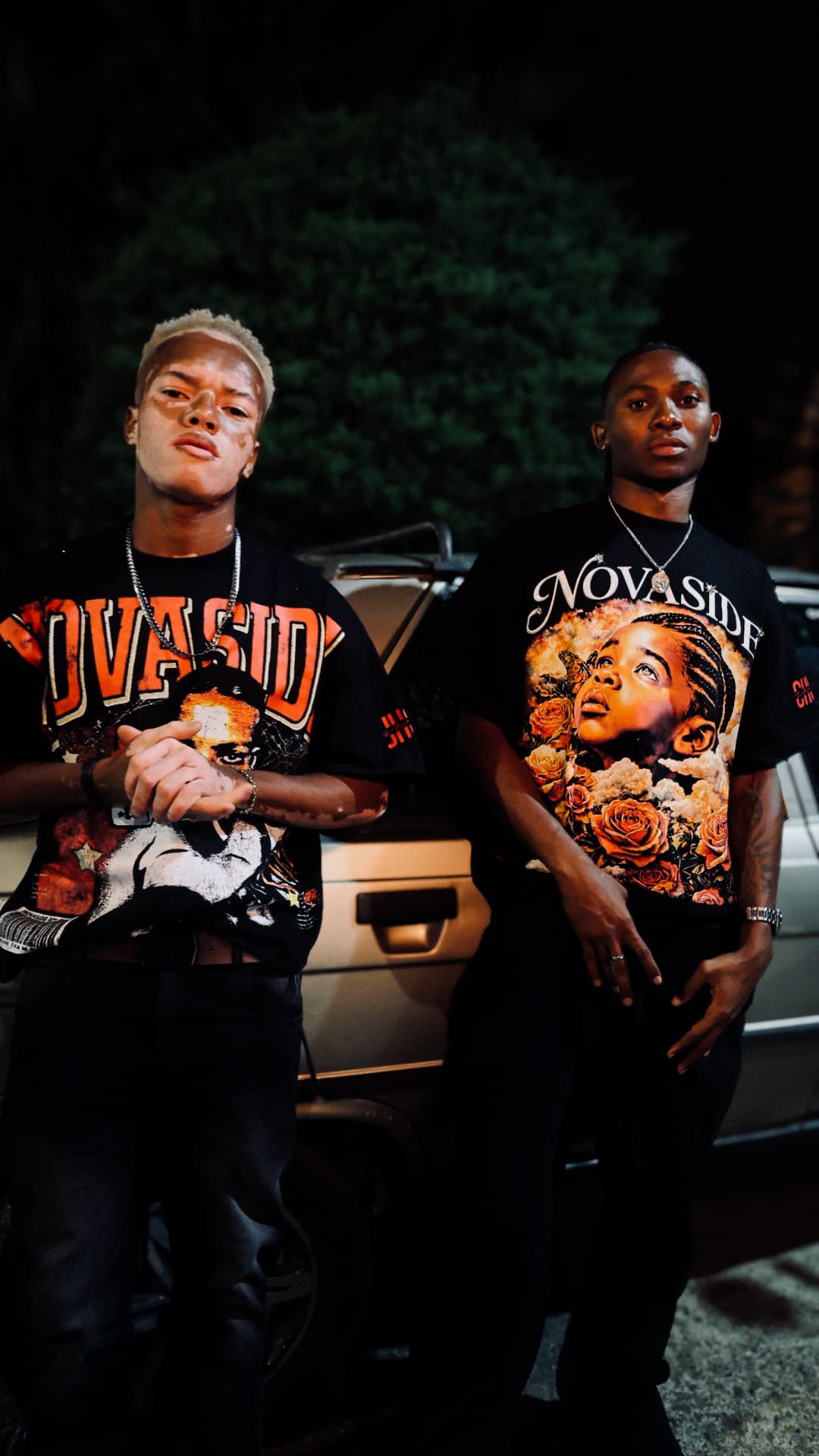Dos modelos con camisetas gráficas NOVASIDE junto a un automóvil